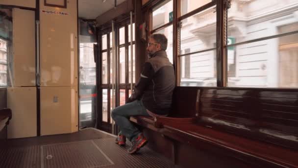 Milán, Itálie-květen 2019: typický italský muž jezdí v retro tramvaji, zatímco sedí na dřevěné lavici. Pojem osamění. Zpomaleně — Stock video