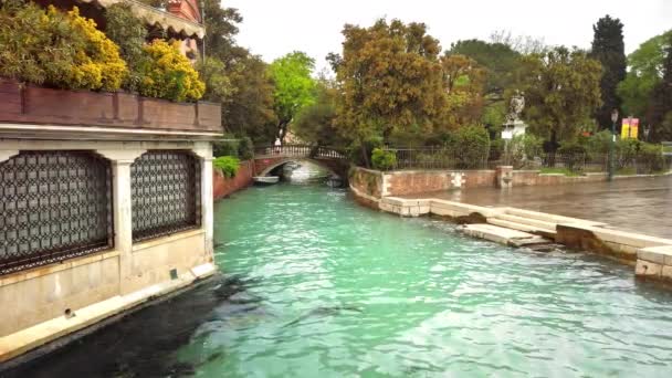 VENECIA, Italia - Mayo 2019: Paisaje romántico con tiempo lluvioso. Un canal con agua azul clara, en la distancia un puente sobre el que pasan personas no identificadas. Movimiento lento — Vídeos de Stock