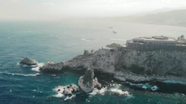 Taormina, Sicilya, İtalya - Ağustos 2019: Okyanus kıyısındaki kayalık bir dağda tanınmayan bir otel tesisi. Köpüklü su dalgaları kayalar. Bir tatil pahalı lüks tatil kavramı. Havadan insansız hava aracı vuruldu