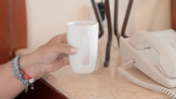 Mujer mayor adulta en un albornoz blanco acostada en una cama en un hotel toma un vaso de agua de una mesita de noche y bebe de ella. Moción lenta — Vídeo de stock