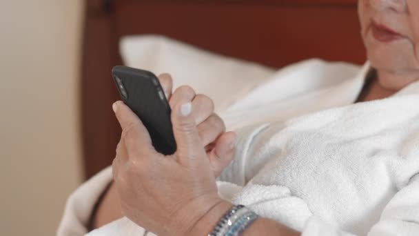Beyaz bornozla tanınmayan yetişkin kadın akıllı telefon kullanarak sohbet mesajları yazarak. Yaş olgun insanlar tarafından teknoloji ve gadget'lar kullanma kavramı. Yavaş Çekim — Stok video