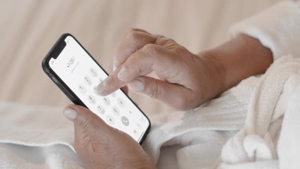 Η μη αναγνωρισμένη ενήλικη γυναίκα με λευκό μπουρνούζι καλεί έναν αριθμό τηλεφώνου σε ένα smartphone. Η έννοια της χρήσης της τεχνολογίας και των gadget από τους ώριμους ανθρώπους της ηλικίας. Αργή κίνηση — Αρχείο Βίντεο