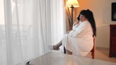 mutlu, gülümseyen Kafkas yaşlı kadın arıyor ve beyaz bir bornoz büyük bir panoramik pencere yakınında oturan bir otelde telefonda konuşuyor. Yaşlı insanlar tarafından gadget'lar kullanma kavramı. Yavaş