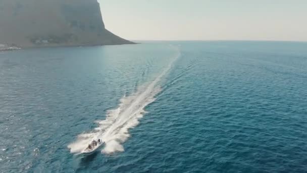 Швидкісний човен з невизначеними туристами проходить через океан. На задньому плані скеля. Концепція прагнення до перемоги та перемоги. Повітряний безпілотник постріл — стокове відео
