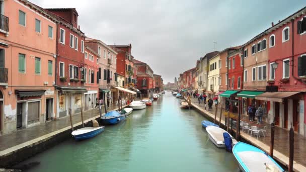 Murano, Venice, Italy-mei 2019: uitgaand waterkanaal waarop de boten afgemeerd zijn. Er zijn bakstenen huizen aan de zijkanten. Regenachtig weer, niet-herkende mensen lopen onder parasols. Slow Motion — Stockvideo