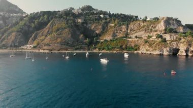Taormina, Sicilya, İtalya - Ağustos 2019: Okyanusun kayalık kıyısına yakın yelkenli yatlar ve tekneler. Havadan insansız hava aracı vuruldu