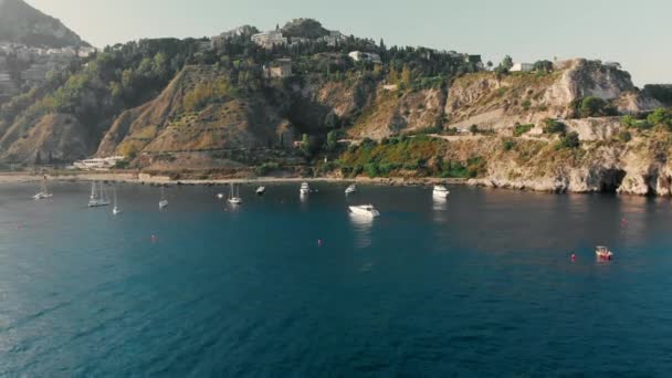 Taormina, SICILIA, Italia - Agosto 2019: Yates de vela y barcos cerca de la costa rocosa del océano. Disparo aéreo con drones — Vídeo de stock