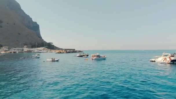 Palermo, SICILIA, Italia - Agosto 2019: muchos turistas en un viaje en barco familiar de verano. La cámara se desliza sobre la superficie del océano de agua turquesa en las montañas de fondo. Hora del atardecer. Disparo aéreo con drones . — Vídeo de stock