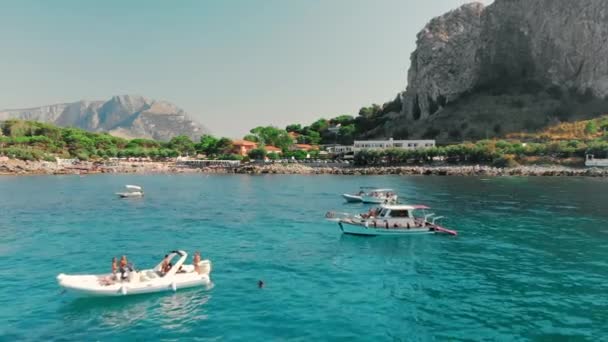 Rest in paradise. Many pleasure boats and sailing yachts off the coast of island. Unrecognized tourists. Clear turquoise water. In foreground is a yacht sailing. Aerial drone shot. Palermo - Italy — Stock Video