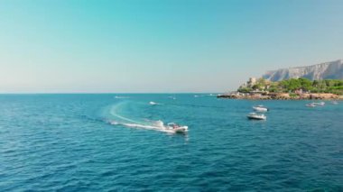 Palermo, Sicilya, İtalya: yüksek hızlı beyaz yolcu teknesi kamera tarafından geçer. Arka planda çok fazla bitki örtüsü ve ağaç olan dağlar. Turkuaz suyu. Deniz tatili konsepti. Havadan insansız hava aracı vuruldu.