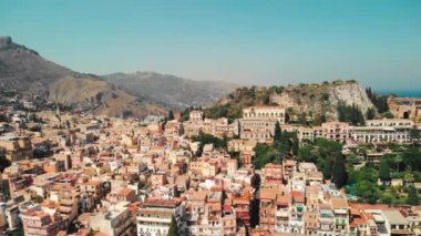Taormina, Sicilya, İtalya - Ağustos 2019: Kayalık dağlar ve yanardağ yakınında kentsel yerleşim. Evlerin ve sokaklarda yürüyen insanların kırmızı çatıları. Havadan insansız hava aracı vuruldu
