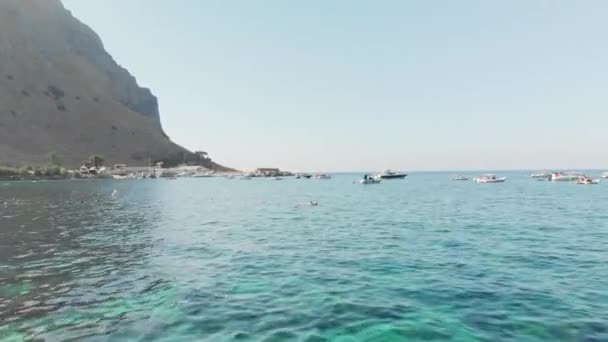 Camera slides over unrecognized people snorkeling in clear water. Seascape, many boats on the background. Aerial drone shot — Stock Video