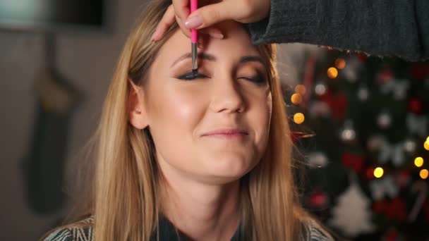 Professionelle Visagistin macht Make-up. zeichnet mit einem Pinsel Ösen. im Inneren für die Weihnachtsfeier dekoriert — Stockvideo