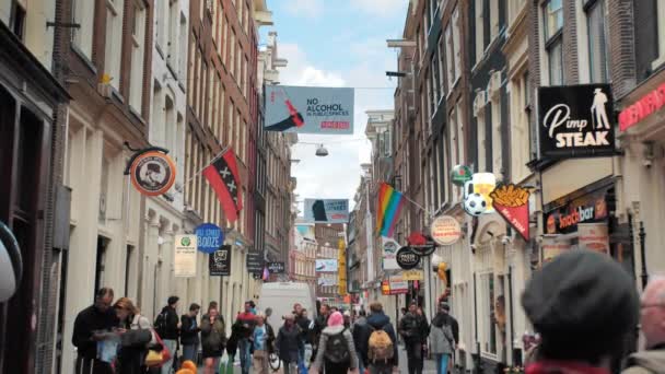 АМСТЕРДАМ, Нидерланды - октябрь 2019: ЛГБТ-флаг и другие разноцветные плакаты на улице в центре Амстердама. Много туристов и местных жителей, движущихся вдоль улицы — стоковое видео