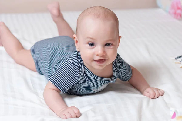 Glückliches süßes Baby liegt auf weißem Laken Stockbild