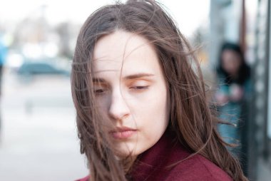 Rüzgarda dalgalanan saçları olan güzel bir genç kadının portresi. Sağlıklı genç bir kadının yakın plan yüzü. Dalgalanan siyah saçlı, düşünceli kız kameraya bakarak rüzgarın tadını çıkarıyor..