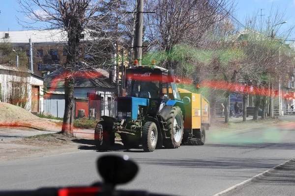 Traktör kapıcısı güneşli bir bahar gününde tozlu bir şehir caddesini temizliyor.