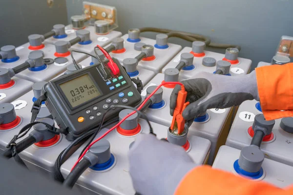 Electrical and instrument technician measuring voltage and internal resistance of battery to monitor performance of electrical system on oil and gas construction platform.
