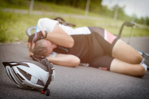 骑自行车躺在路上 拿着他的头 头盔在前景 — 图库照片