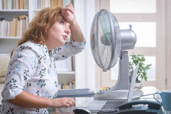 女人在办公室里工作时感到很热 所以尽量靠著风扇凉快一点 — 图库照片