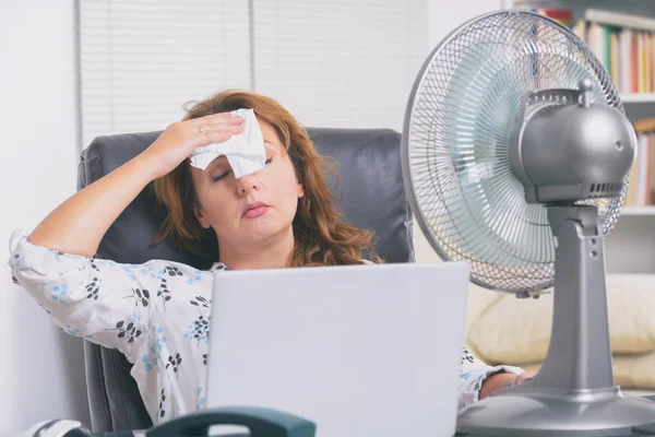 女人在办公室里工作时感到很热 所以尽量靠著风扇凉快一点 — 图库照片