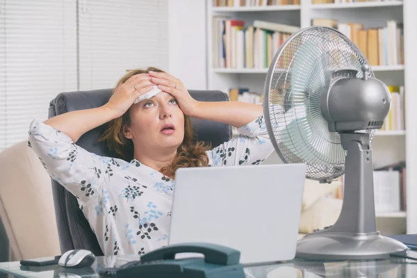 女性はオフィスで働いている間に熱に苦しみ ファンによって冷却しようとします — ストック写真