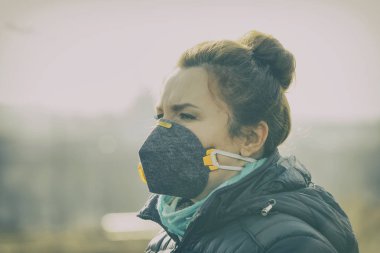 Woman wearing a real anti-pollution, anti-smog and viruses face mask; dense smog in air. clipart