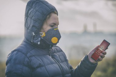 Woman wearing a real anti-pollution, anti-smog and viruses face mask and checking current air pollution with smart phone app clipart