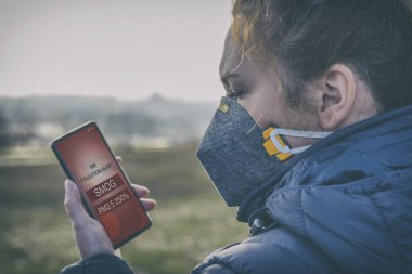 Gerçek anti-çevre kirliliği, Anti-smog giyen kadın ve virüs yüz maskesi ve akıllı telefon uygulaması ile Şu anki hava kirliliği kontrol