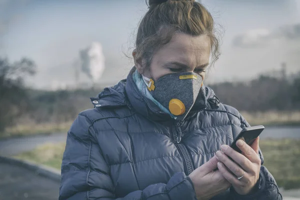 Woman wearing a real anti-pollution, anti-smog and viruses face mask and checking current air pollution with smart phone app