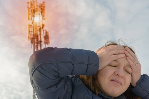 The woman is holding her head near the BTS. Harmful radiation from cellular network transmitters concept