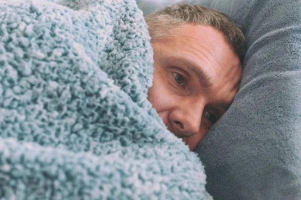 中年の男性がうつ病に苦しんである彼のベッドに毛布で覆われて悲しいことに — ストック写真
