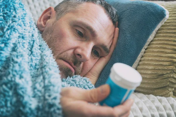 患抑郁症的成熟男人悲哀地躺在床上 床上铺着一条毯子 手里拿着一瓶抗抑郁药 — 图库照片