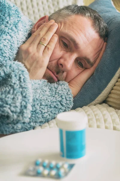 うつ病に苦しむ熟女は悲しいことに彼のベッドの上に毛布で覆われているとテーブルの上に抗うつ薬を見て — ストック写真