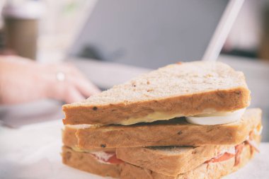 Kadın laptopla çalışırken kahvaltı sandviçi yiyor.