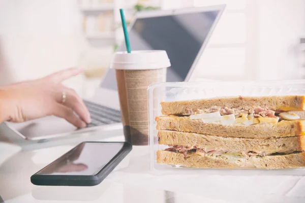 Женщина ест сэндвич с завтраком во время работы с ноутбуком — стоковое фото