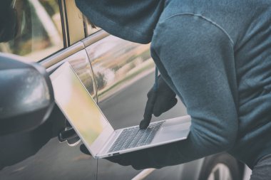 Kapüşonlu hırsız arabanın güvenlik sistemini lapt ile kırmaya çalışıyor.