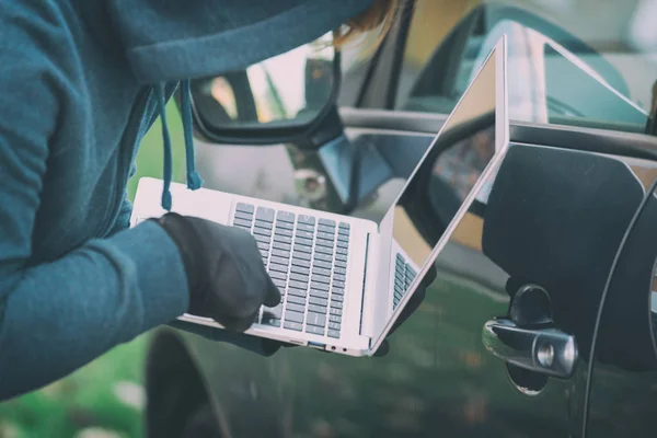 Ladrón encapuchado intenta romper los sistemas de seguridad del coche con lapt — Foto de Stock