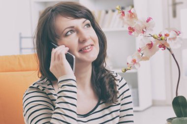 Akıllı telefondan konuşan kadın koltukta oturuyor.