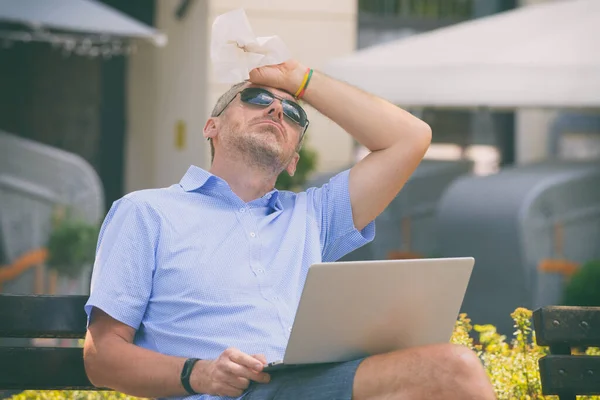 Mężczyzna Cierpi Ciepło Podczas Pracy Laptopem Zewnątrz Wycierając Czoło Chusteczką — Zdjęcie stockowe