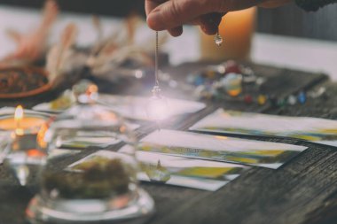 Falcı tarot kartlarının üzerinde sarkacı tutuyor.