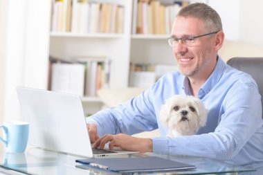 Adam evde çalışıyor ve küçük köpeğini tutuyor..