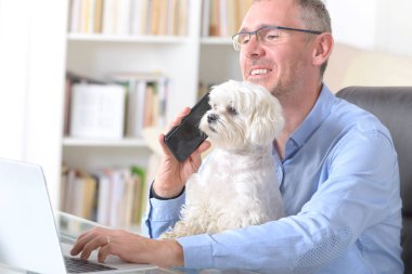 Adam evde çalışıyor ve küçük köpeğini tutuyor..