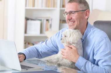 Adam evde çalışıyor ve küçük köpeğini tutuyor..