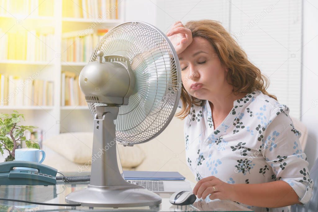 Woman suffers from heat while working in the office and tries to cool off by the fan