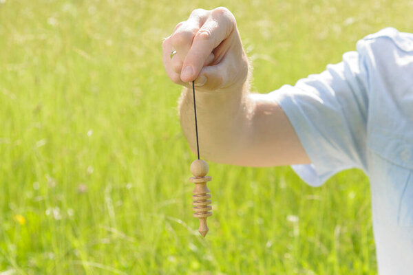Hand with pendulum, tool for dowsing.