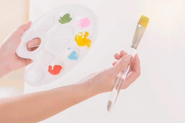 ワークショップスタジオで異なる塗料や絵筆でパレットを保持する女性アーティストの手 — ストック写真