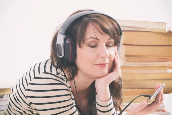 Vrouw Luisterend Naar Een Audioboek Smartphone Zittend Tussen Stapels Papieren — Stockfoto