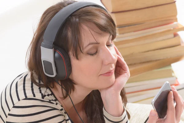 Žena Poslouchá Audioknihu Smartphonu Mezi Hromadami Papírových Knih Podlaze — Stock fotografie
