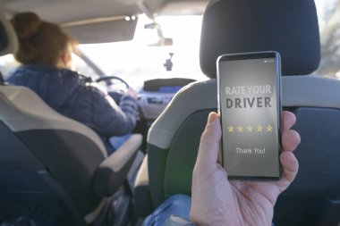 Yolcu arabanın arka koltuğunda oturuyor ve bir sürücüyü değerlendirmek için akıllı telefon uygulamasını kullanıyor. Taksi ya da akran paylaşım konsepti için modern akran